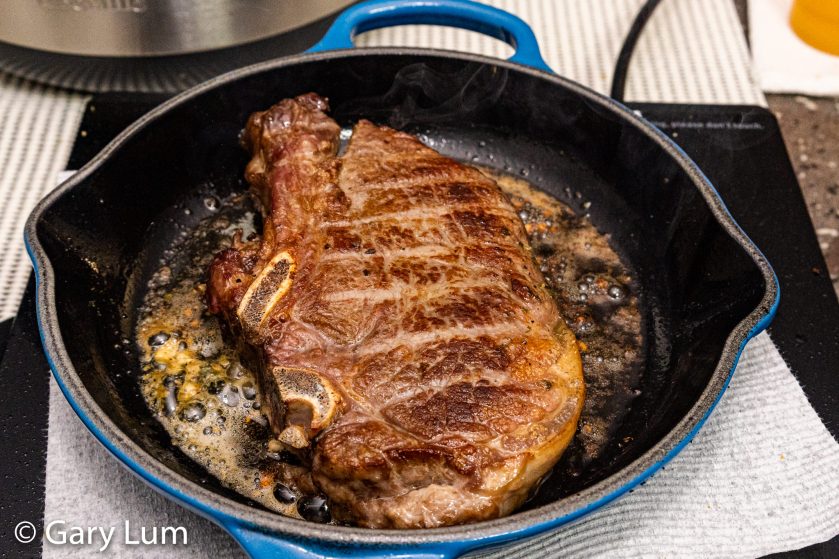 Bone-in rib eye reverse searing in a cast-iron skillet on an induction hob